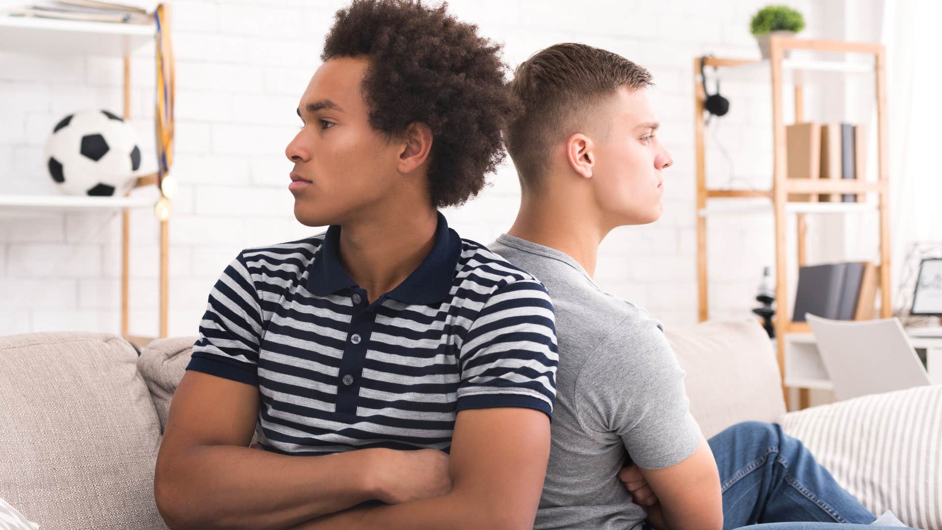 Two male friends looking upset sitting back to back.