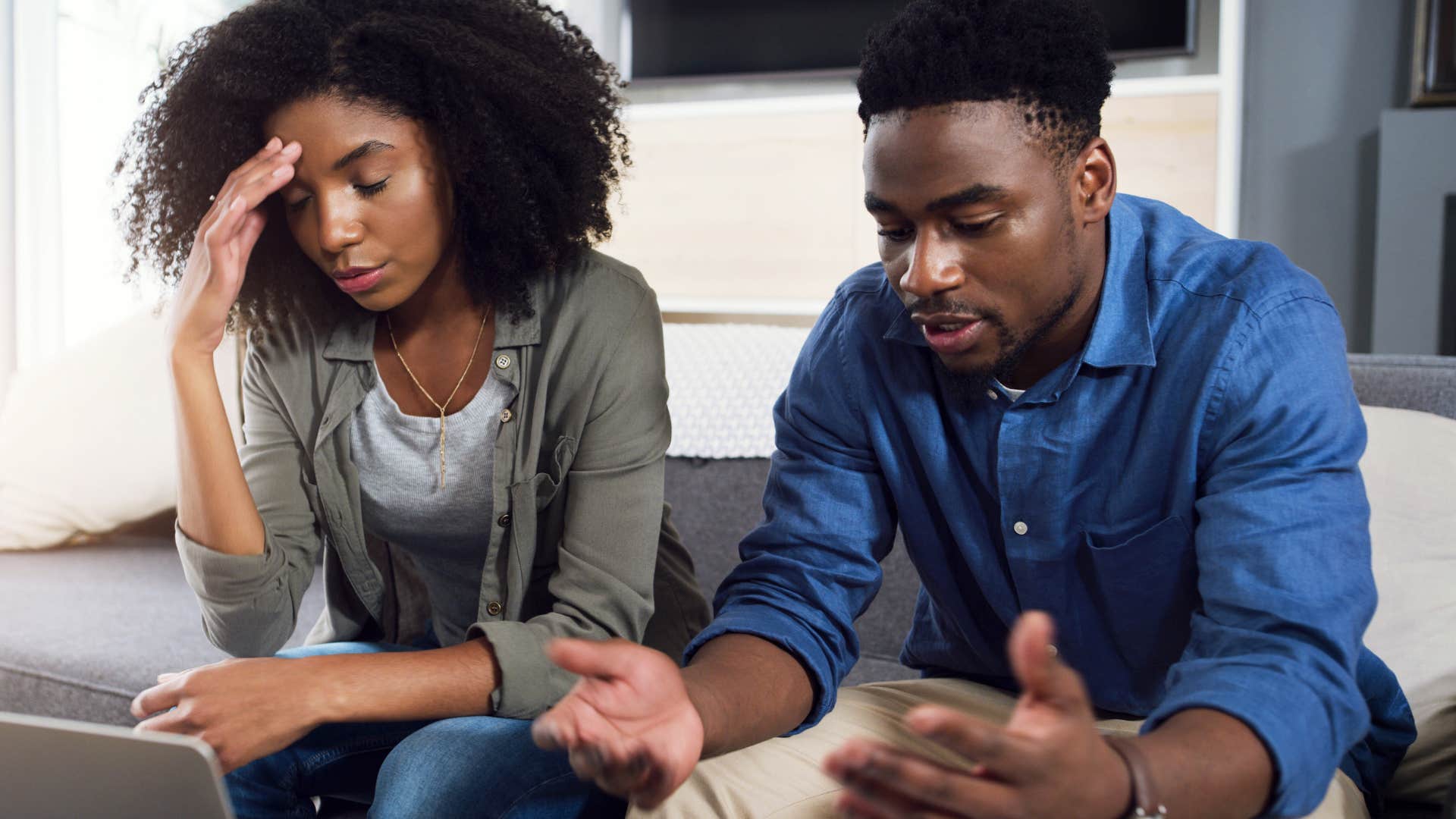 Couple arguing and looking tired sitting on the couch.