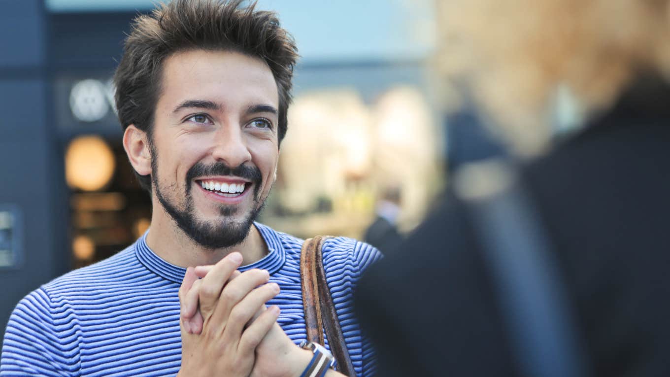 Smiling man holding his hands together and talking to a woman.