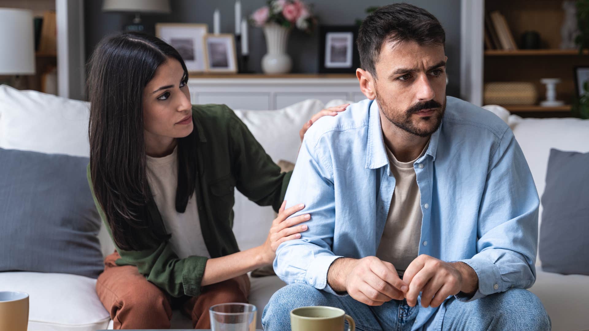 Woman comforting her upset partner on a couch.