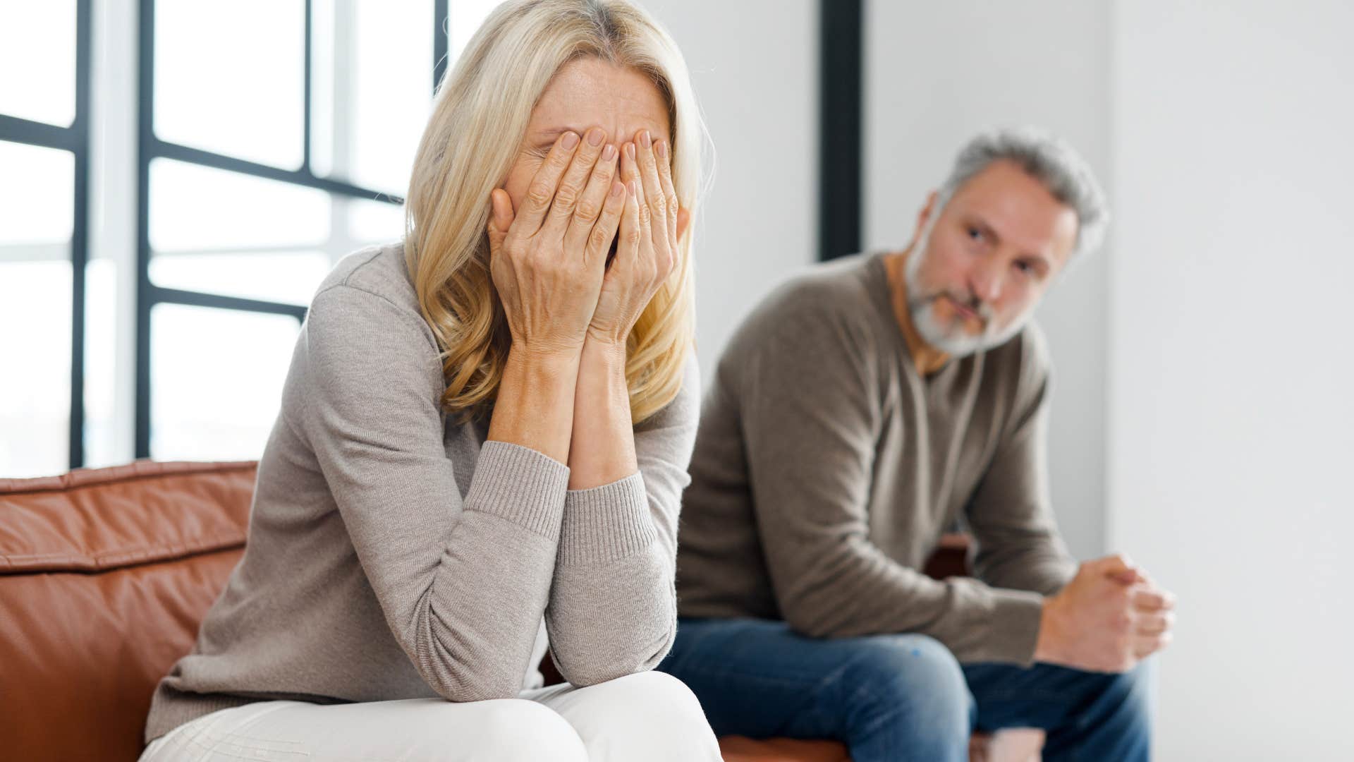 Sad woman with her face in her hands sitting next to her husband.