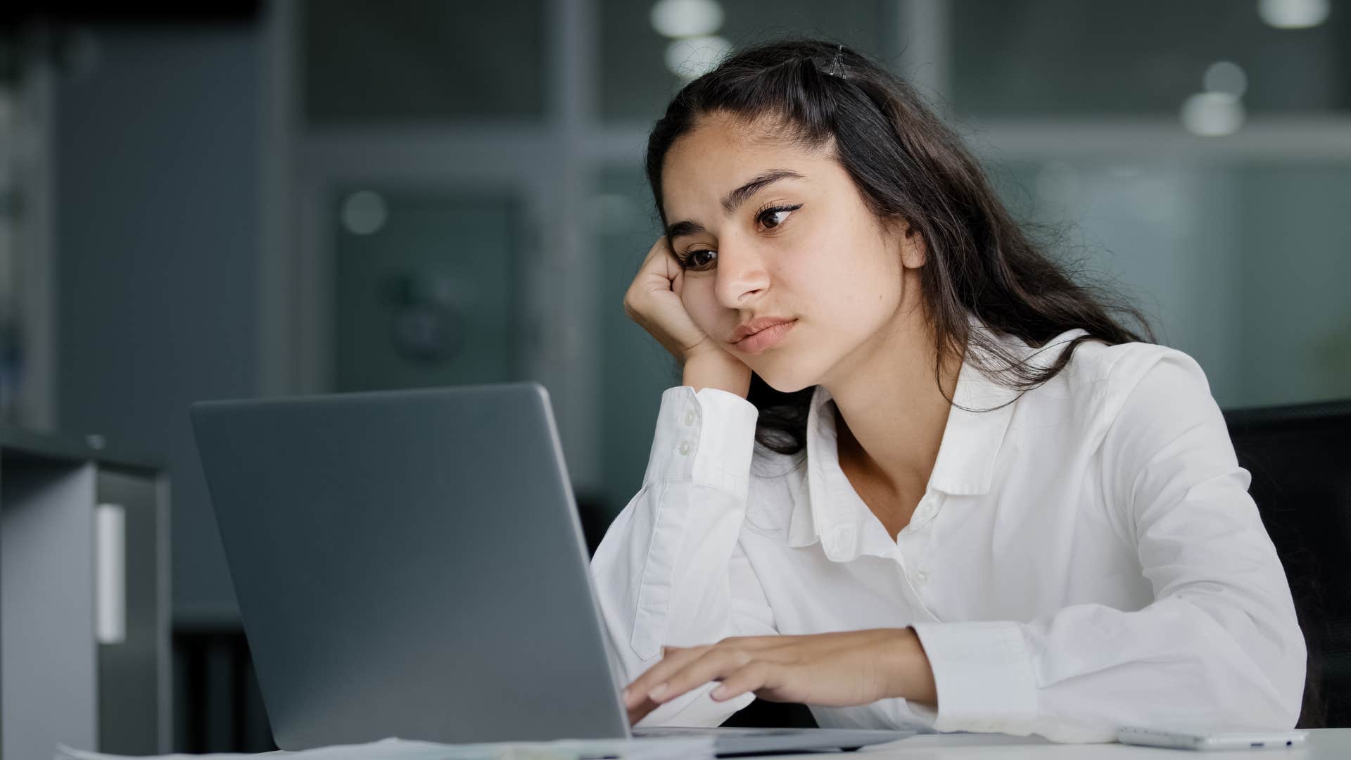 Woman looking annoyed working on her laptop.