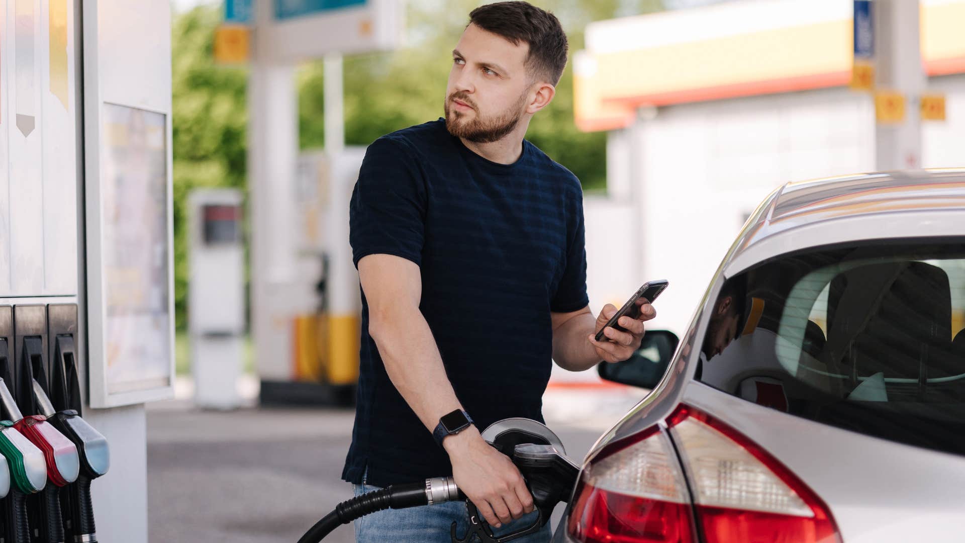 Man looking annoyed pumping gas in his car