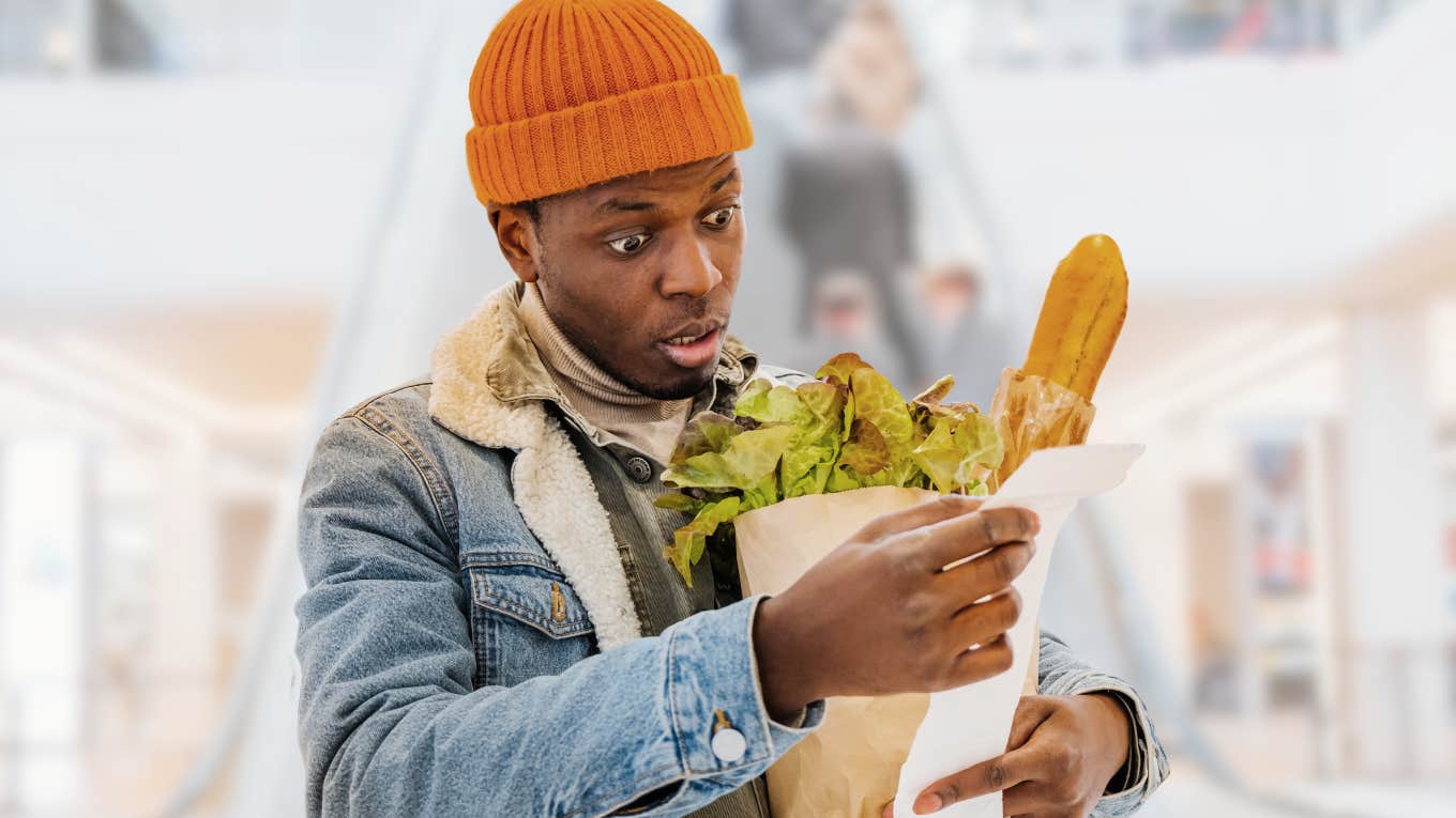 Young man looking shocked staring at his grocery store receipt. 