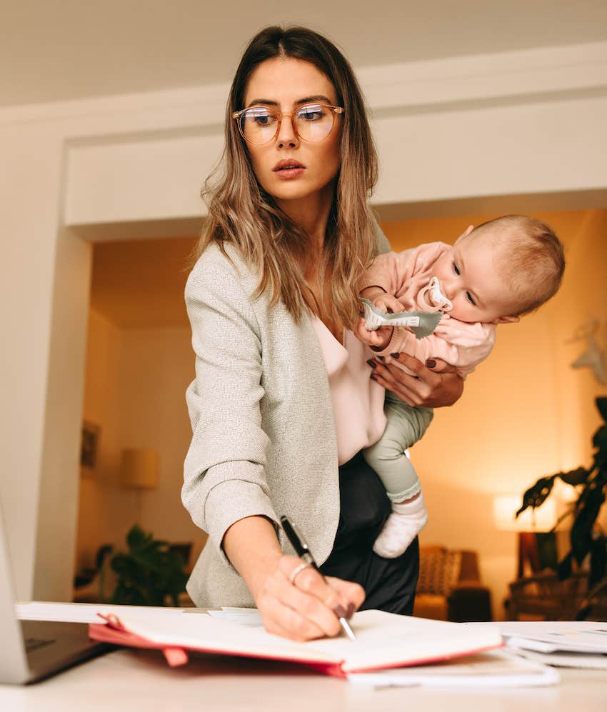 Productive woman holds baby and does paperwork while standing