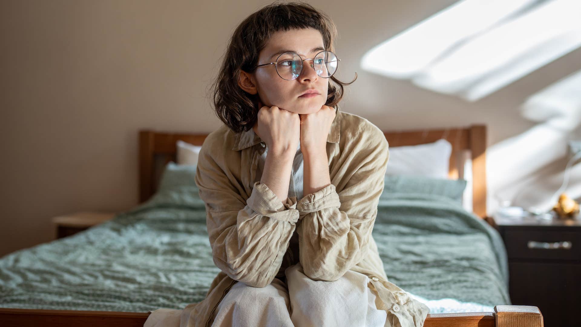 Sad woman sitting on her bed looking out the window.