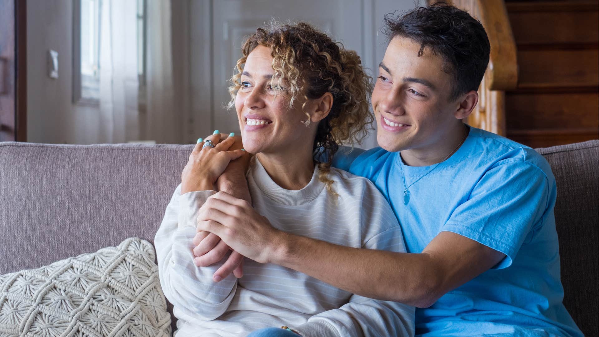 Teenage son hugging his mom and looking out a window.