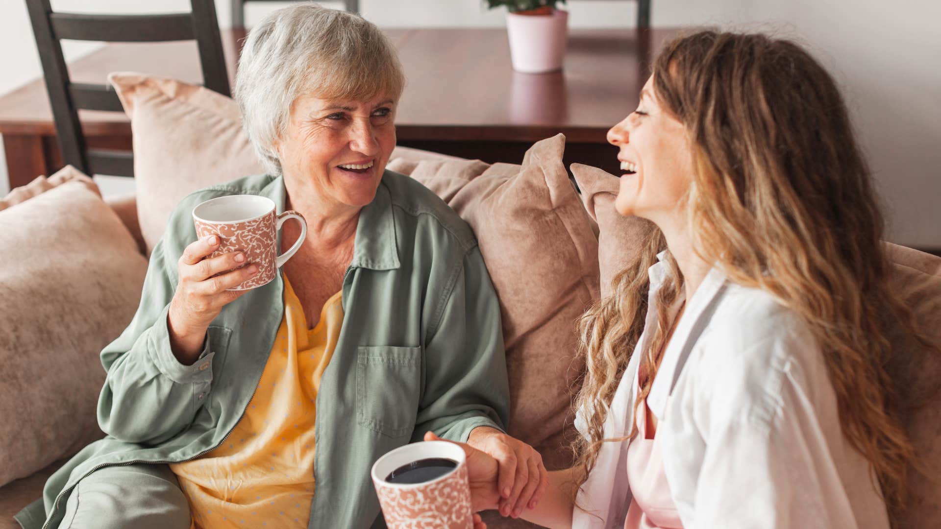 Adult woman smiling and drinking coffee with her mom at home.