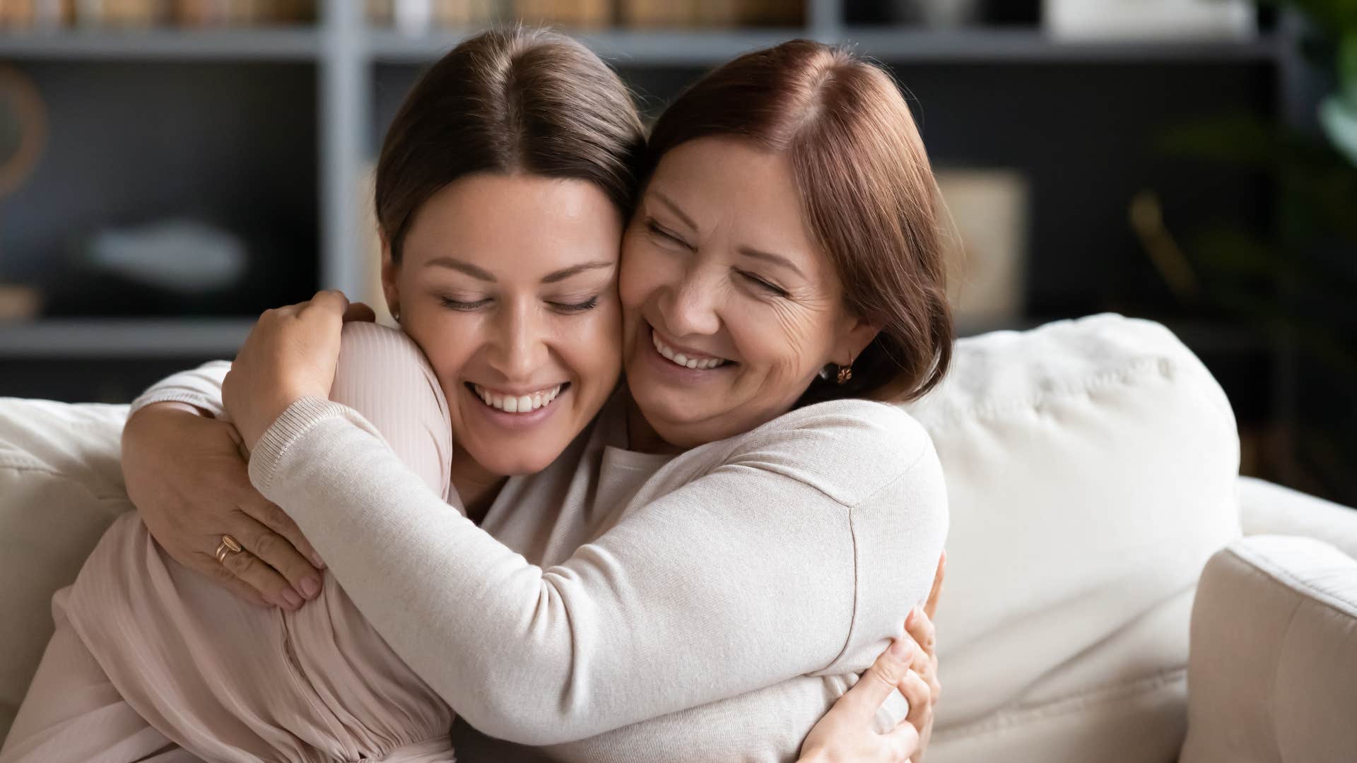 Adult daughter hugging her smiling mom on the couch.