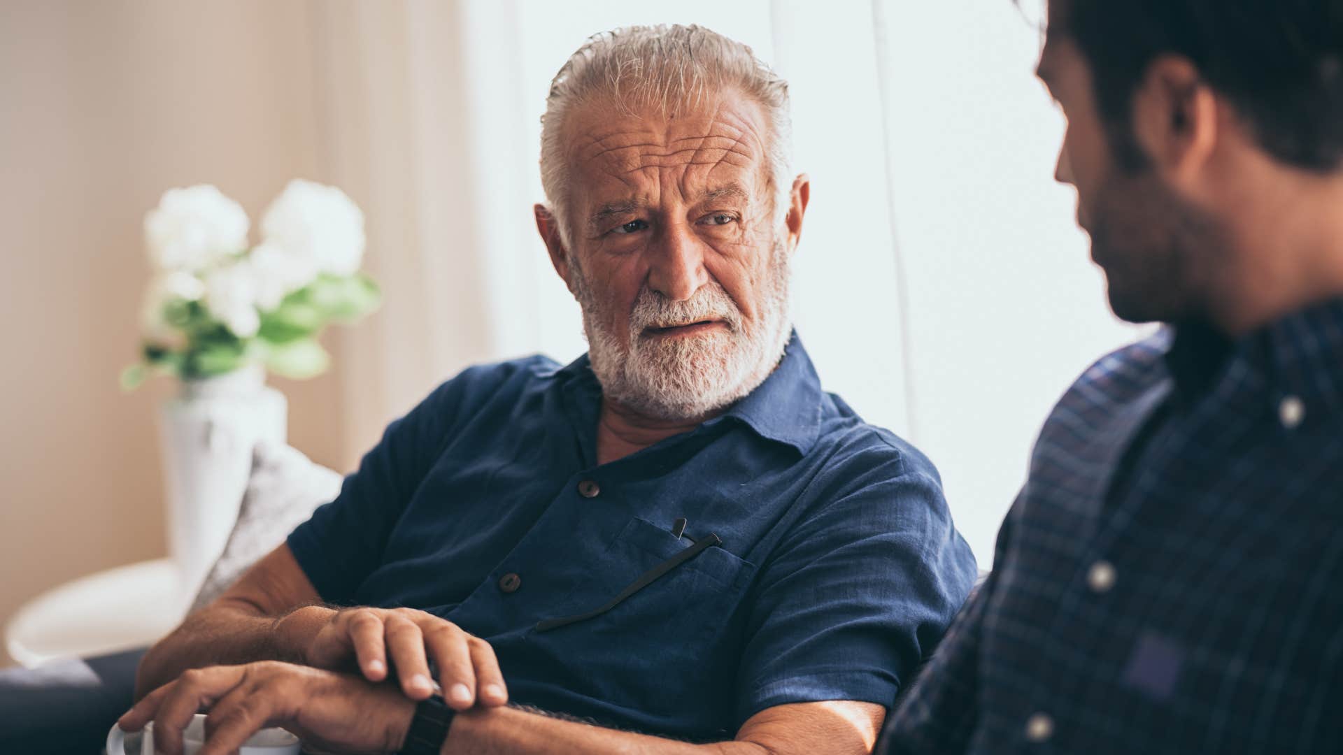 Adult son talking to his upset father on the couch.