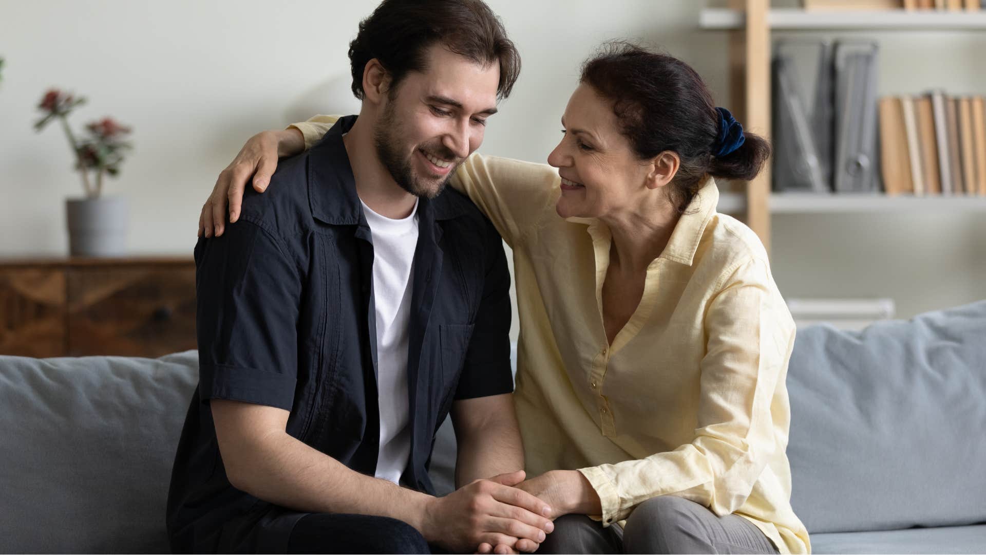 Adult son smiling and holding his mom's hand.