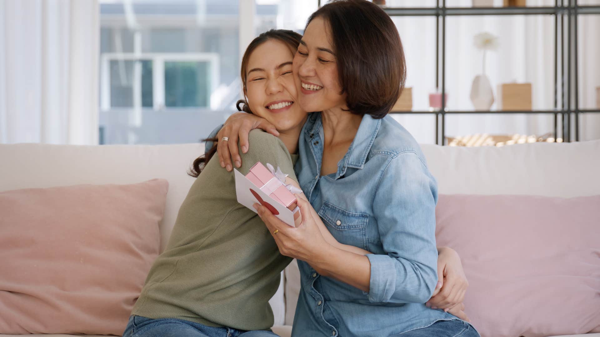 Adult woman hugging her smiling mom on the couch.