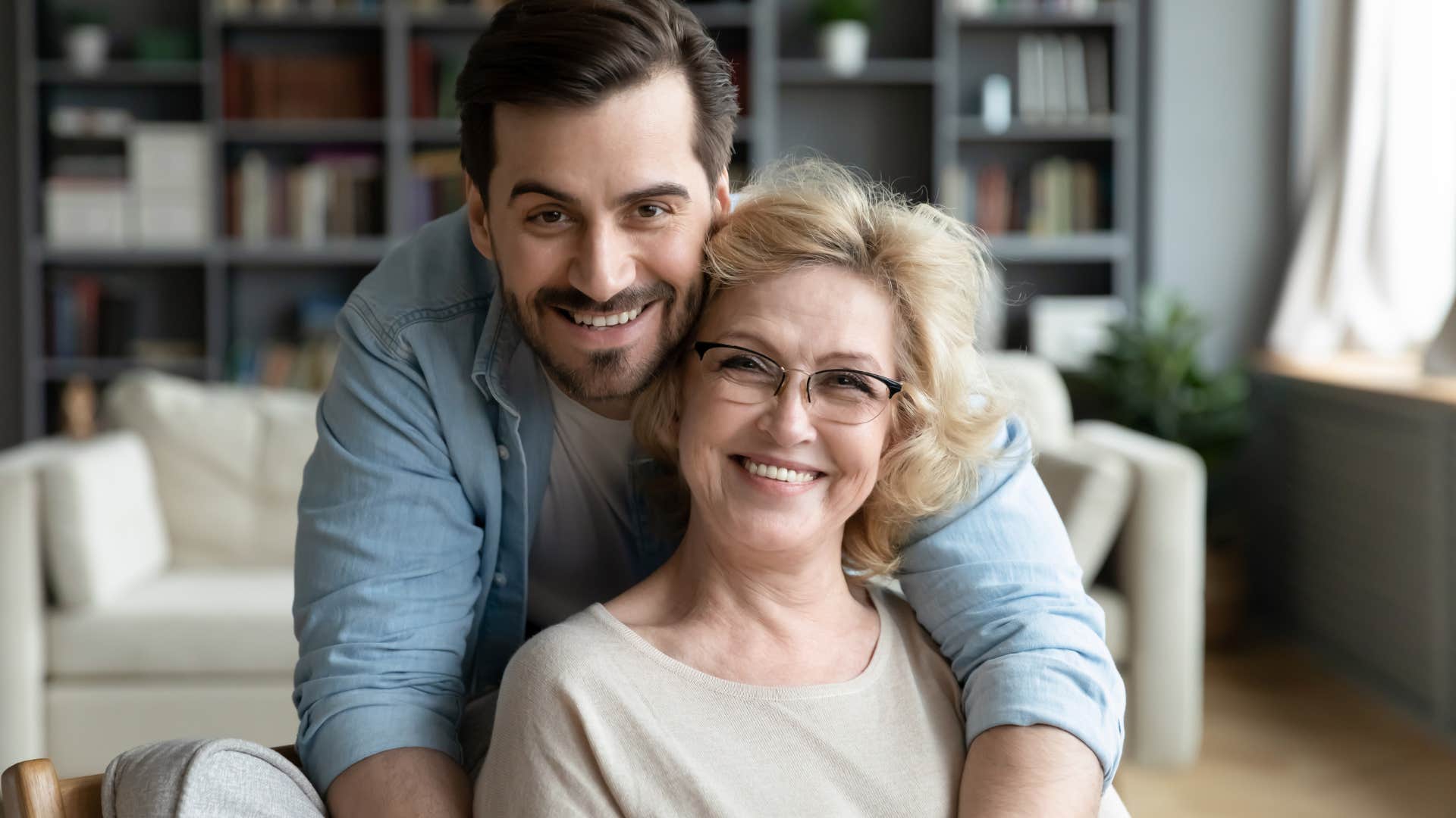 Adult son hugging his happy mom on the couch.