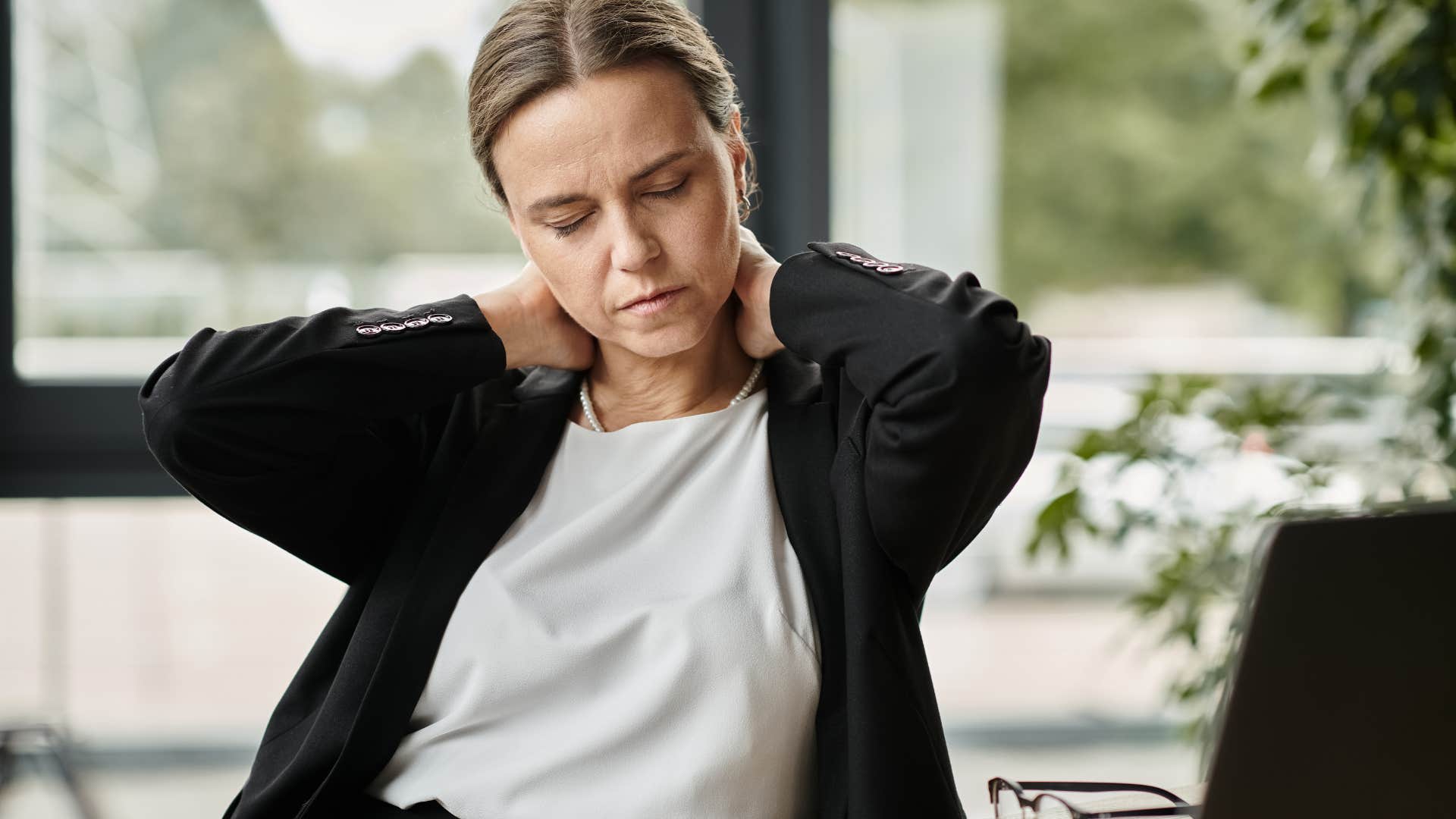 Gen X woman looking tired holding her neck at work.