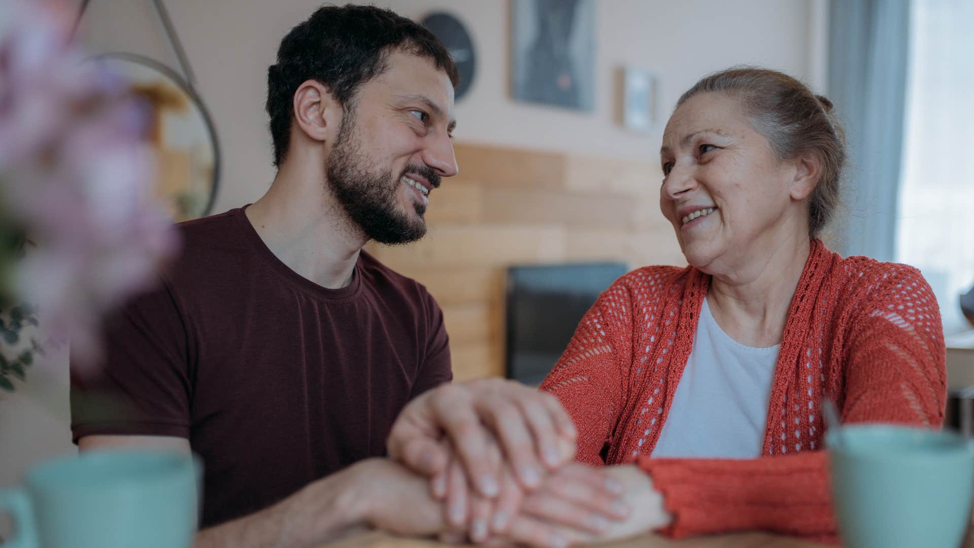 Gen X man smiling and sitting with his older mom at a table