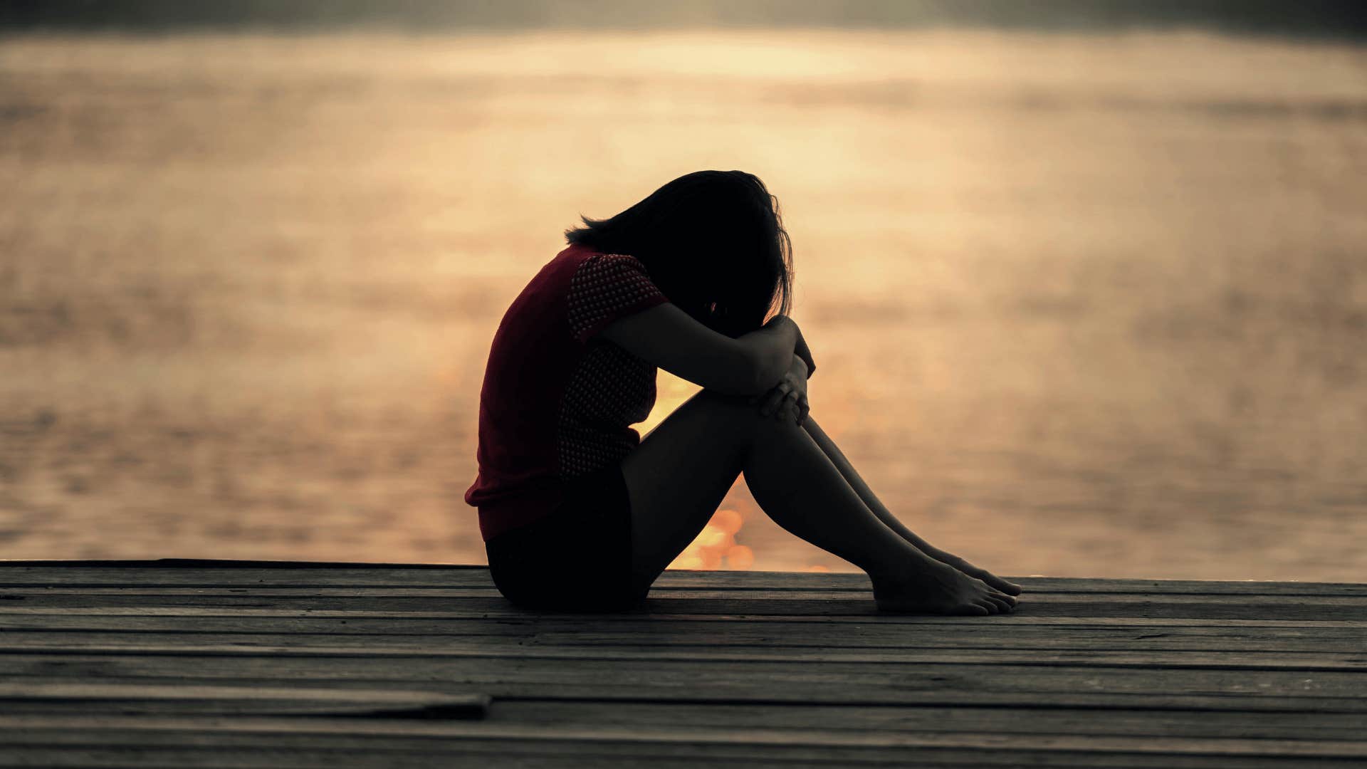 sad woman sitting on dock next to water