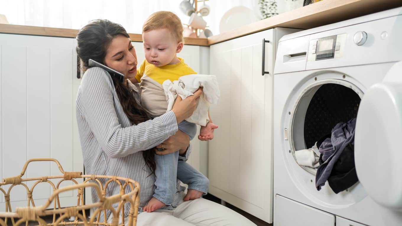 mom trying to do laundry while talking on the phone and holding toddler