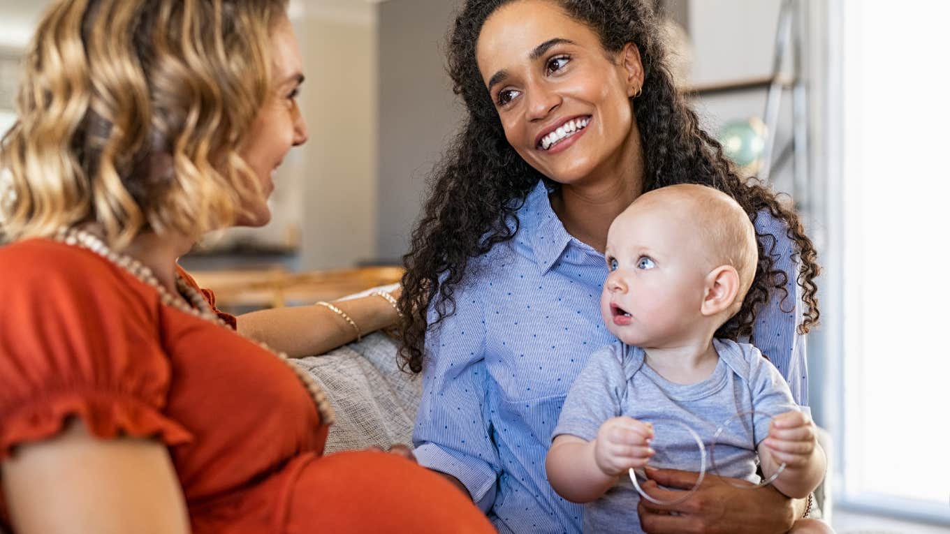 Mixed race woman with expecting mother talking and playing with baby