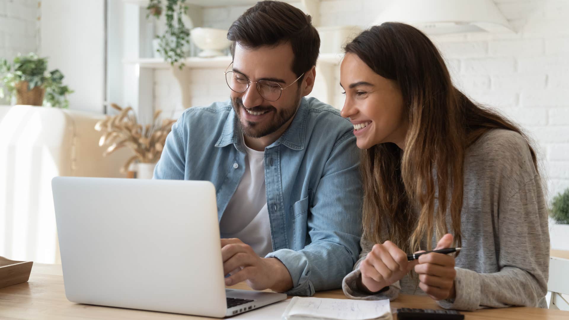 Man smiling with his wife typing on his laptop.