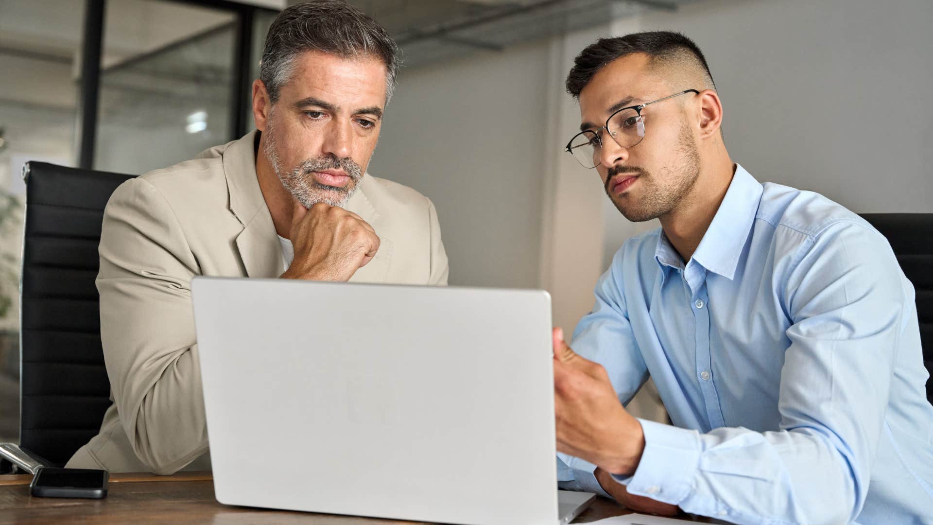 Boss showing his male employee something on his laptop.