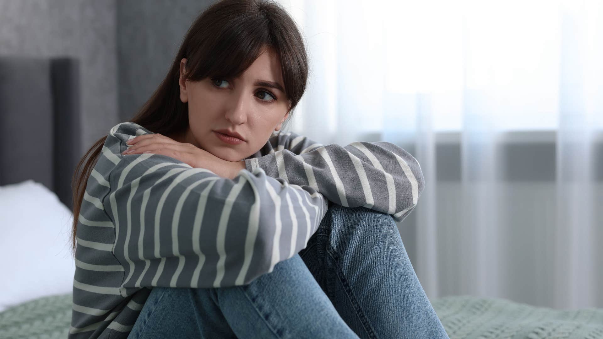 Adult woman looking sad sitting on her bed.