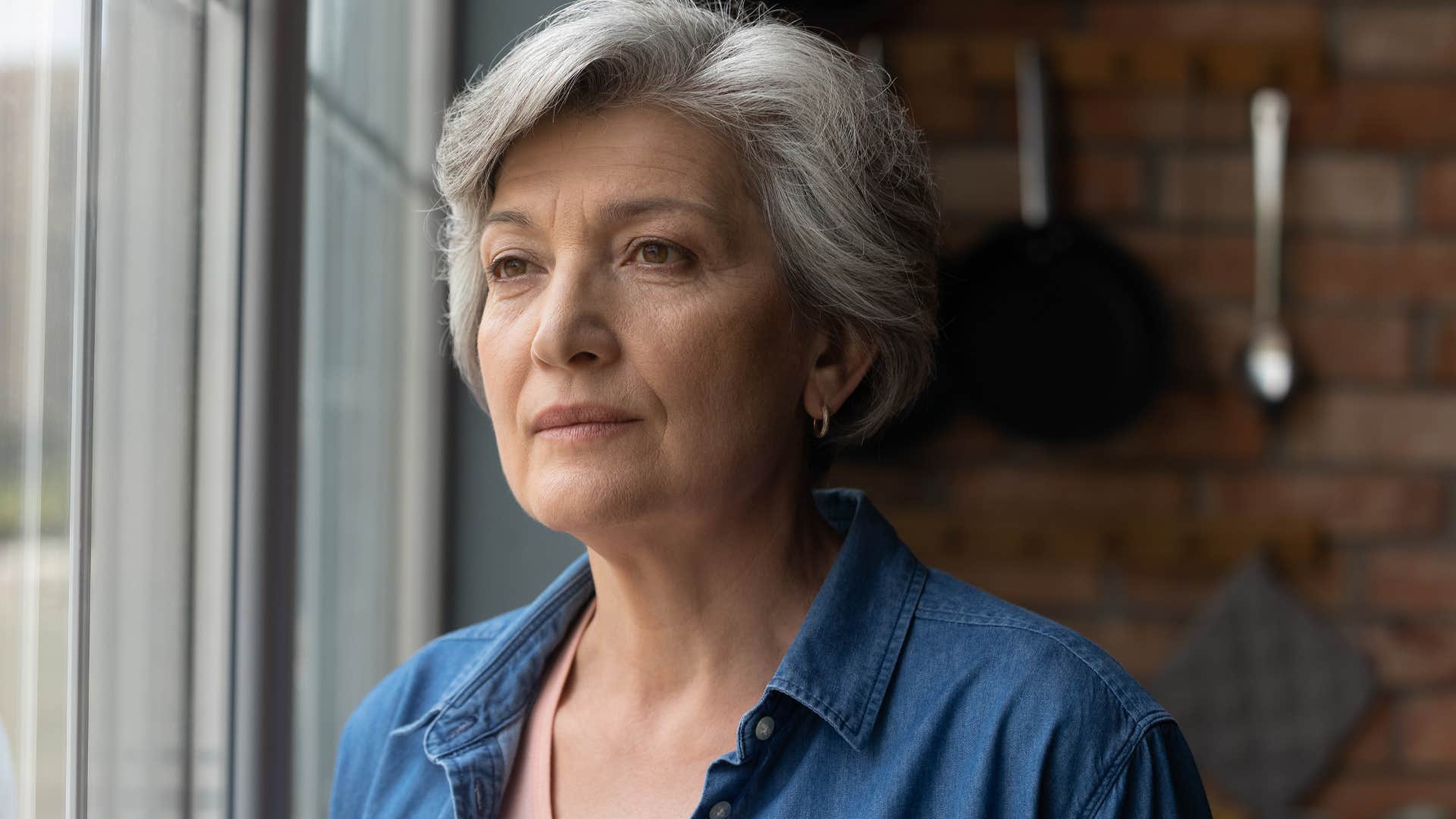 Older woman looking out the window upset