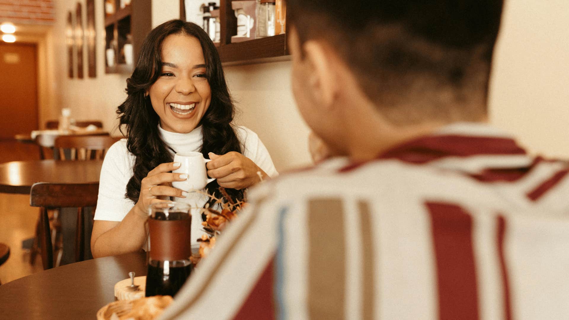 woman laughing with coffee in her hand sitting across from a man