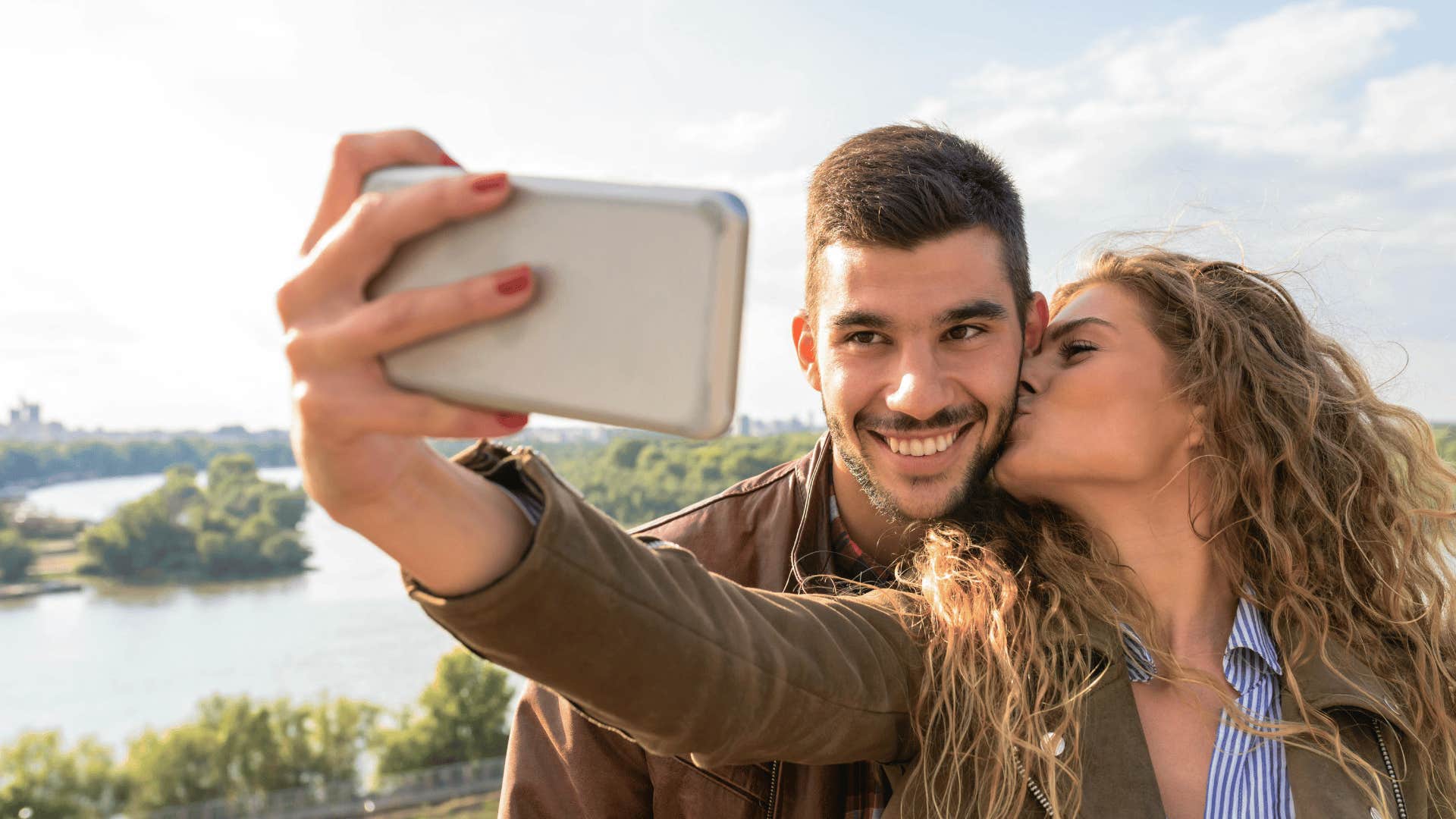 woman kissing man on cheek while taking a photo