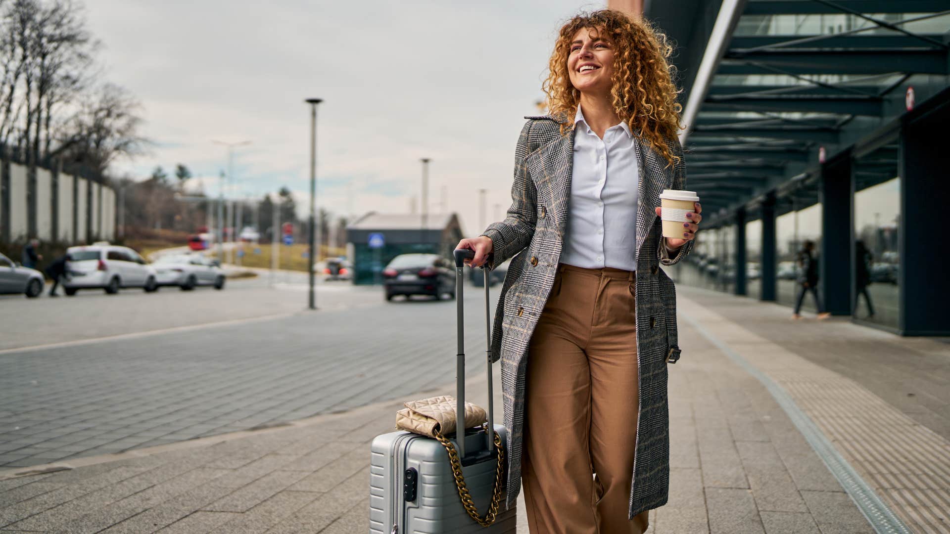 Woman smiling and walking outside with a suitcase