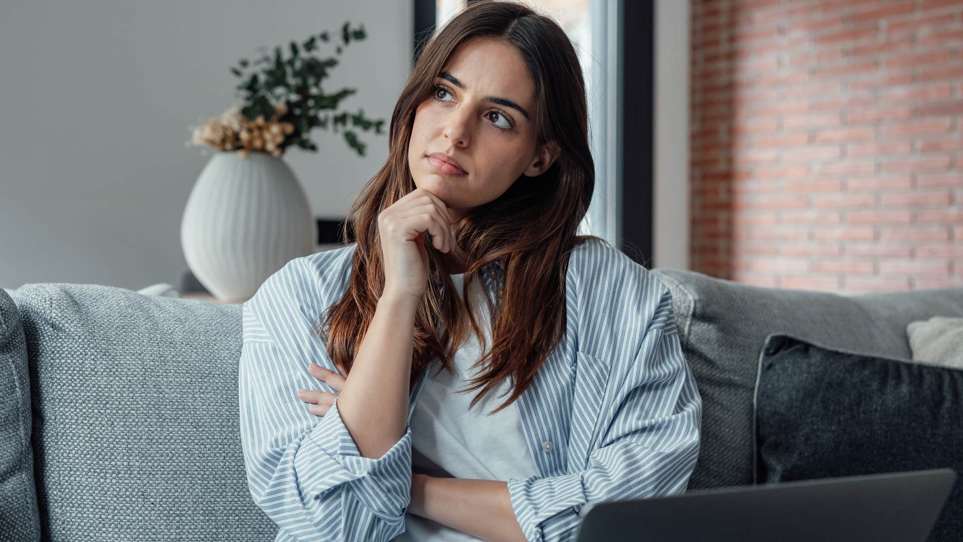 Woman looking away from her laptop on the couch