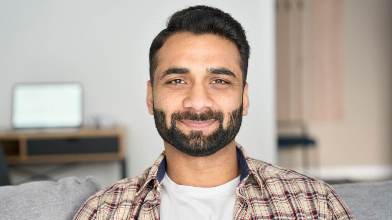 Headshot portrait of confident man looking at camera sitting on couch at modern living room