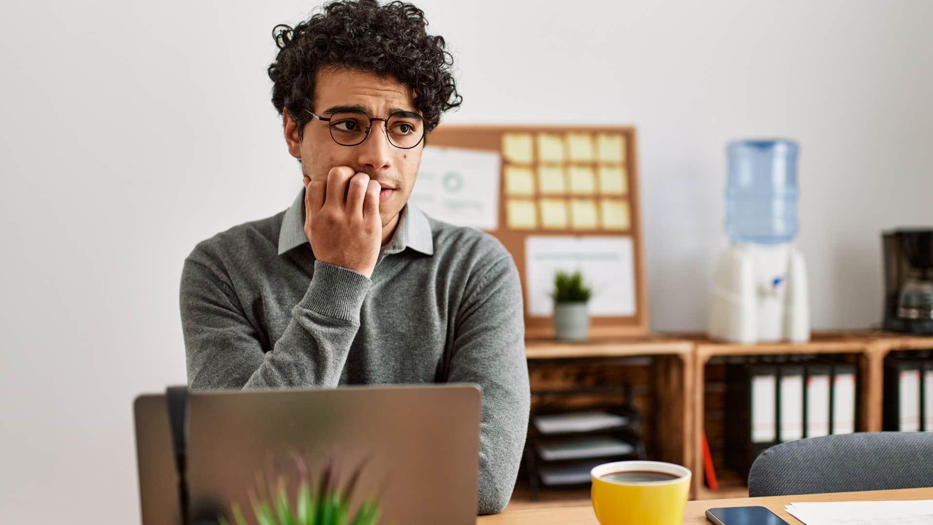 Man biting his nails and looking nervous at his desk.