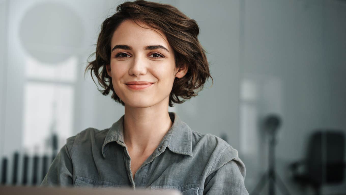 Image of young joyful woman smiling while working with laptop in office