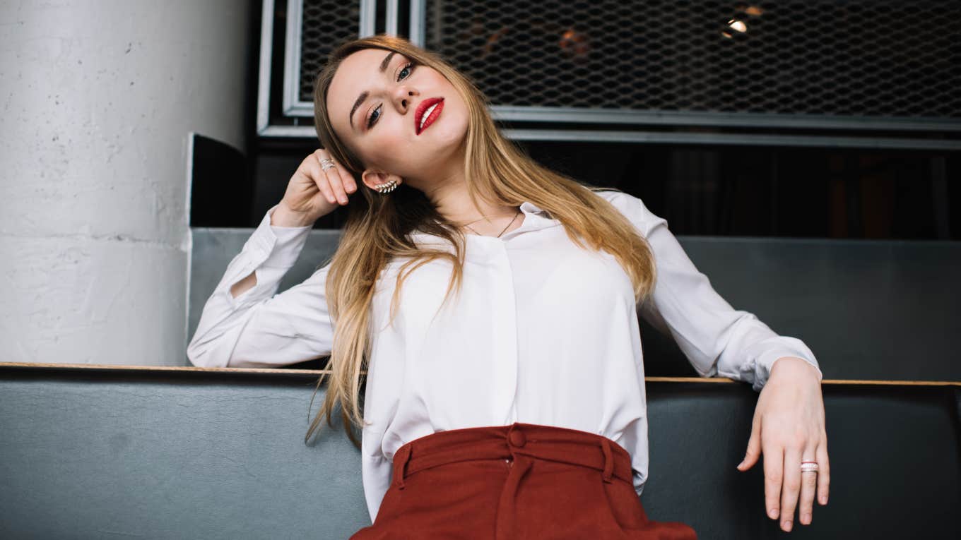 Low angle of serious woman in smart outfit sitting on modern leather couch