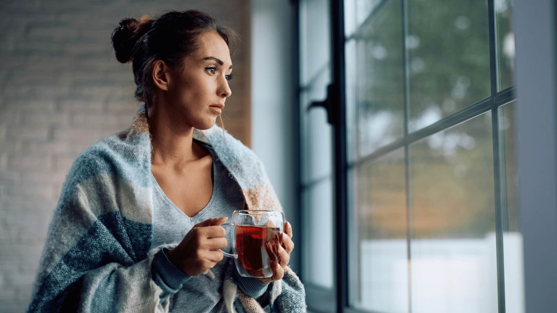 woman looking out of window with tea in her hands 