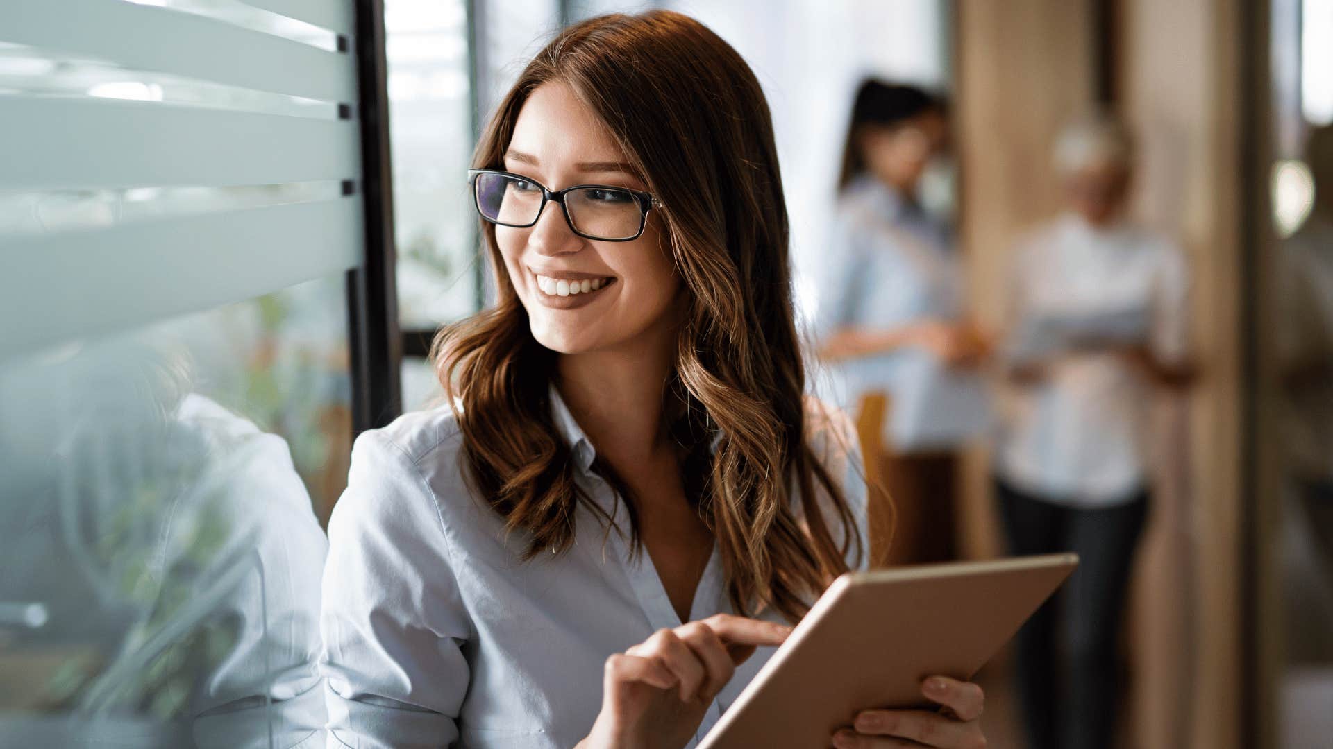 woman smiling while looking out the window and holding tablet 