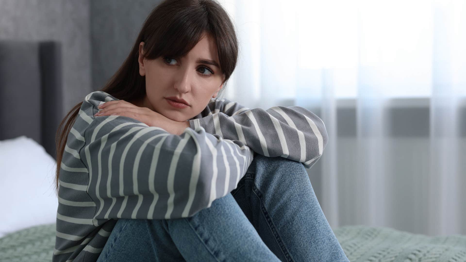 Young woman looking sad sitting on her bed