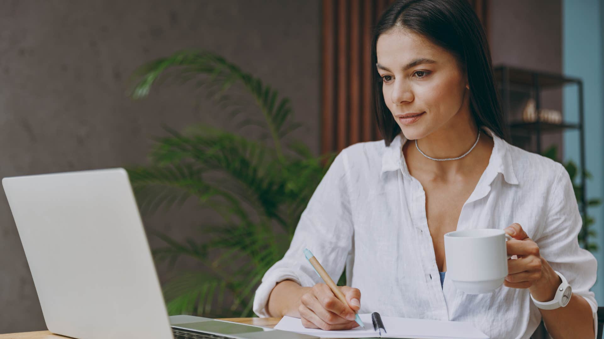 Woman sitting at her desk drinking a mug of coffee.