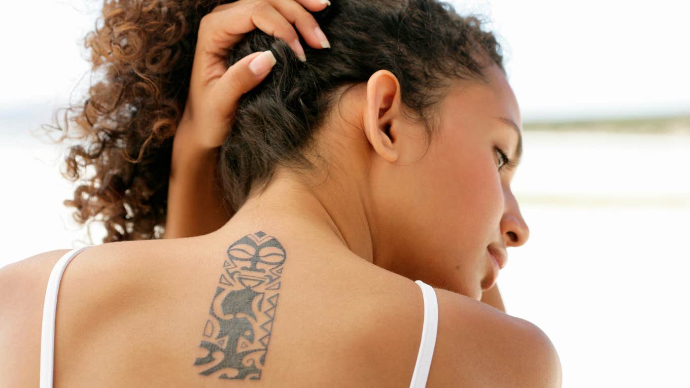 Woman holding hair up, showing back tattoo.