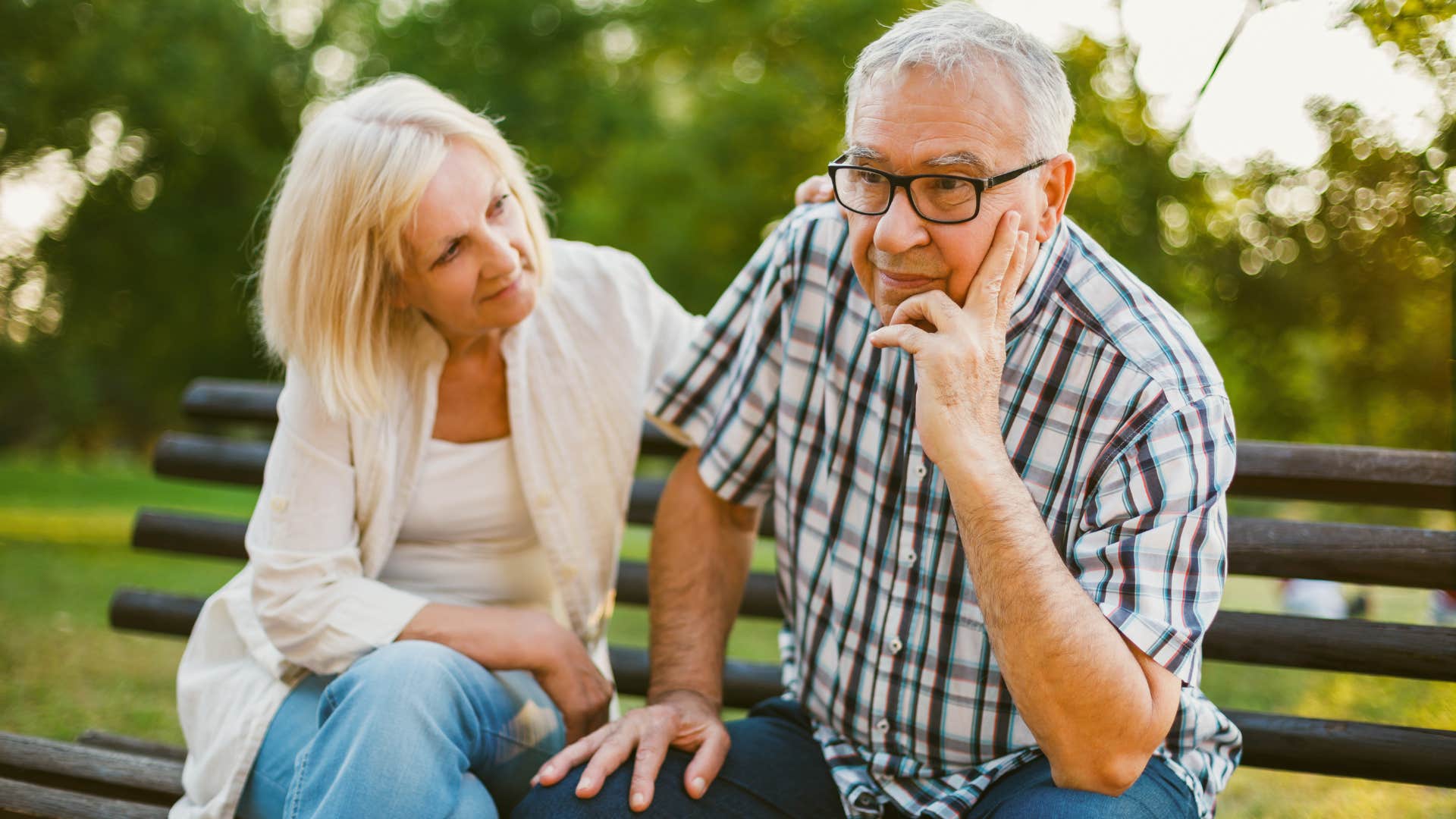 Older couple looking upset sitting on a park bench.