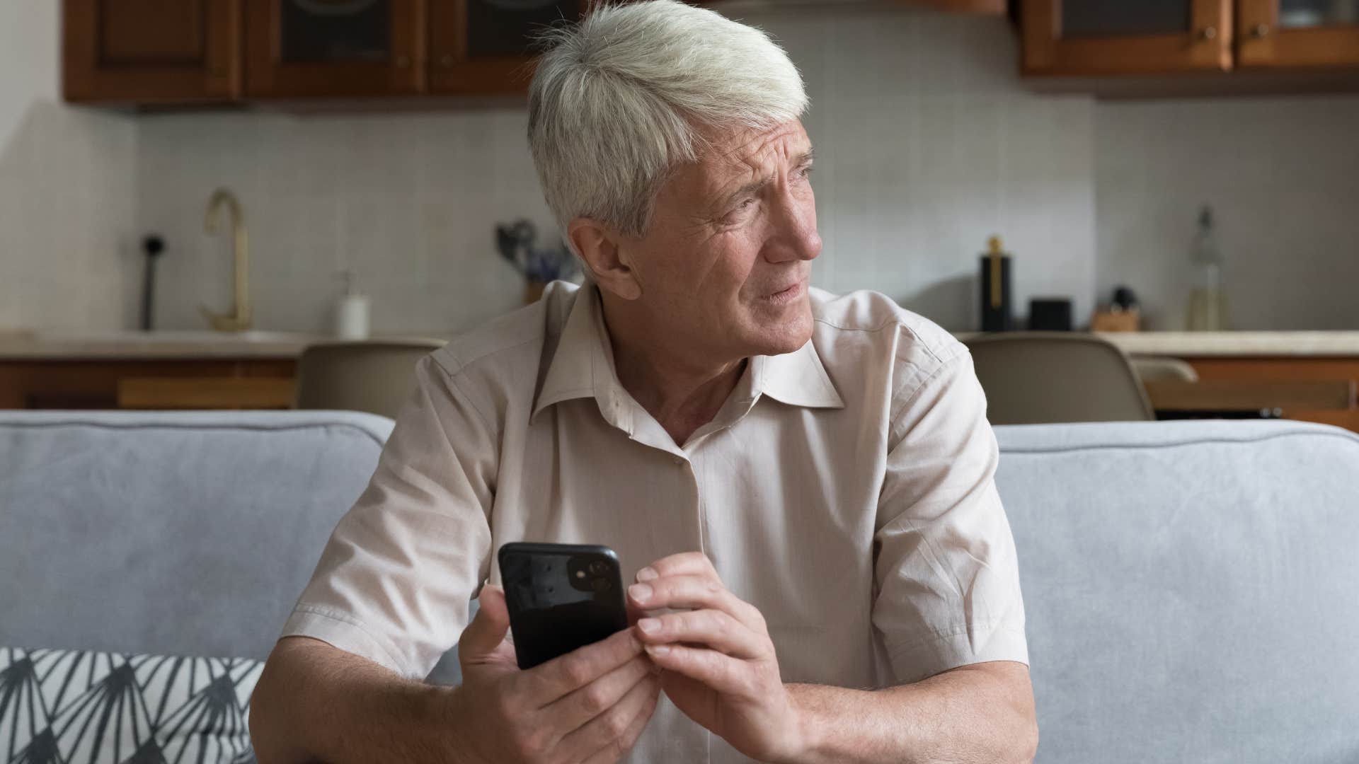 Older man looking confused holding his cell phone.