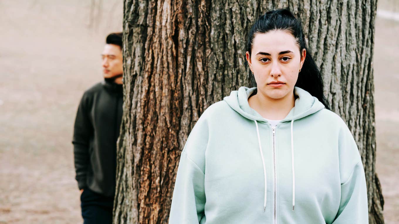 Unhappy adult woman standing by tree. 