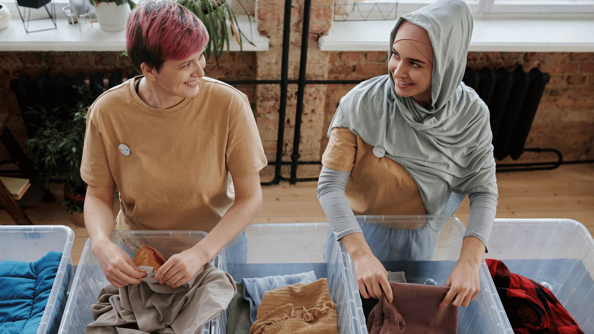 two women smiling at each other in front of bins of clothes