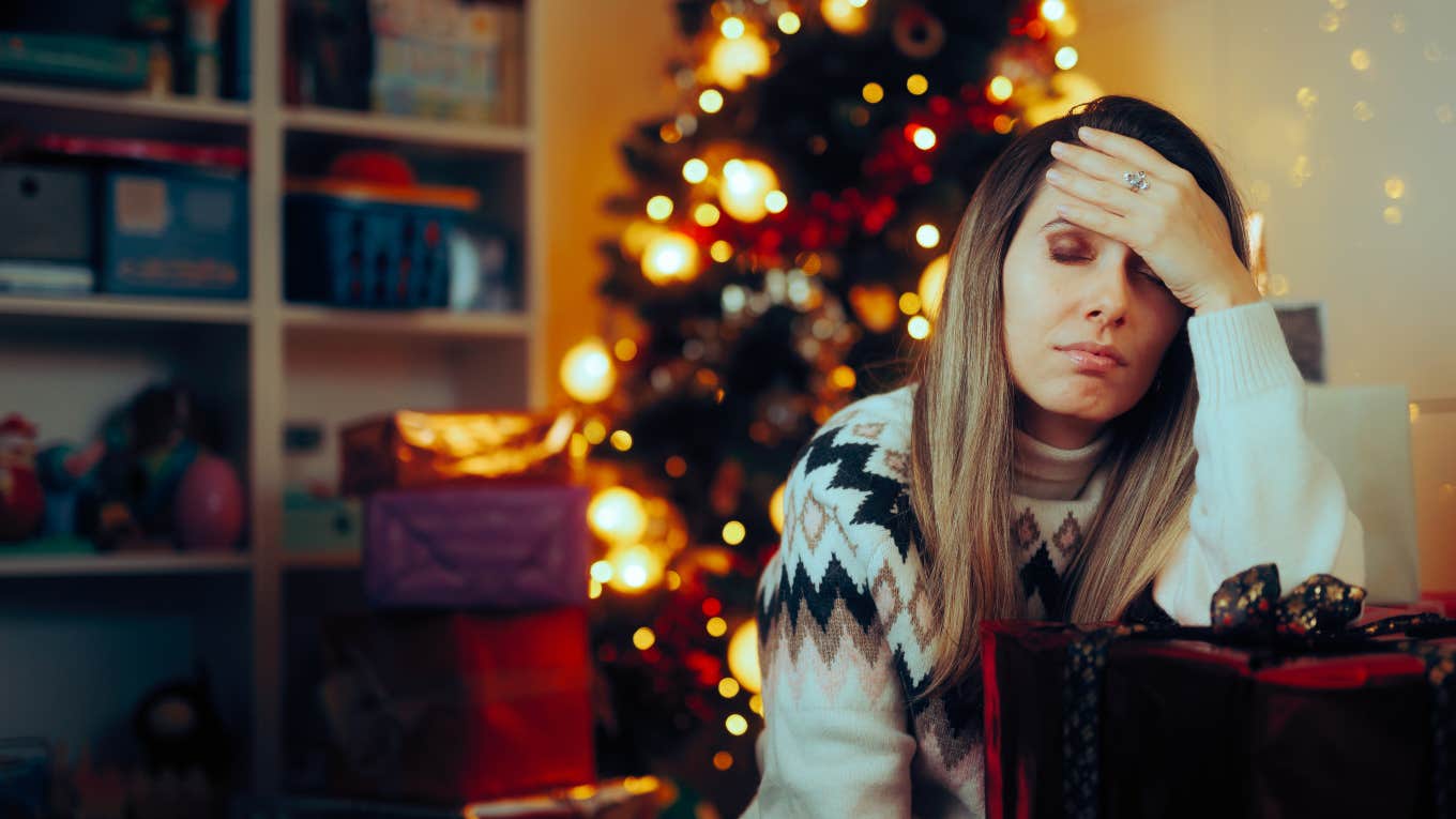 tired, stressed mom sitting around gifts in front of Christmas tree