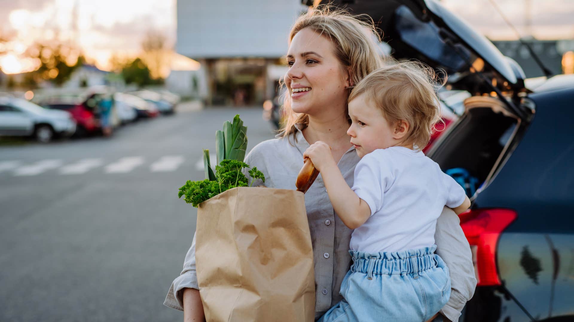 Woman standing in the parking lot with groceries and her baby