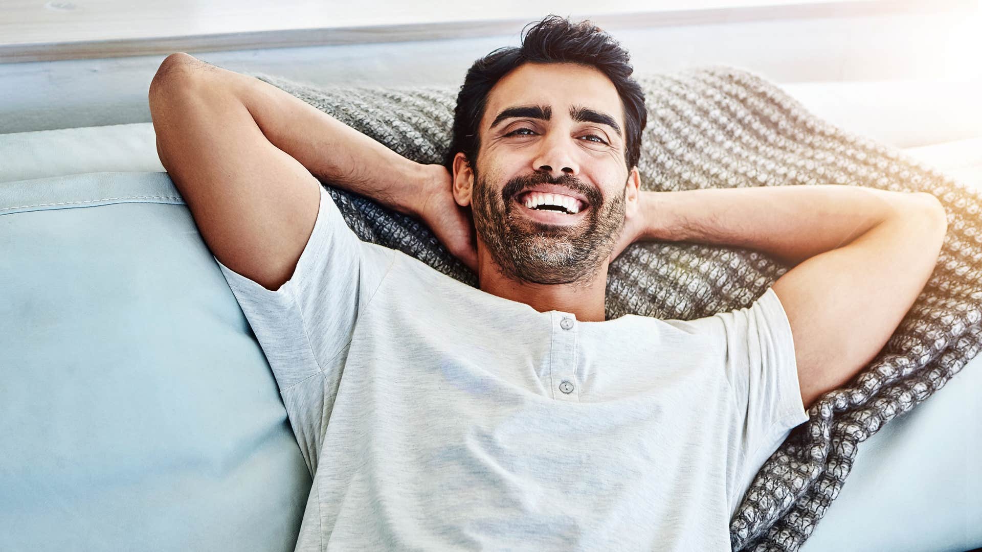 Man smiling and laying with his hands behind his head. 