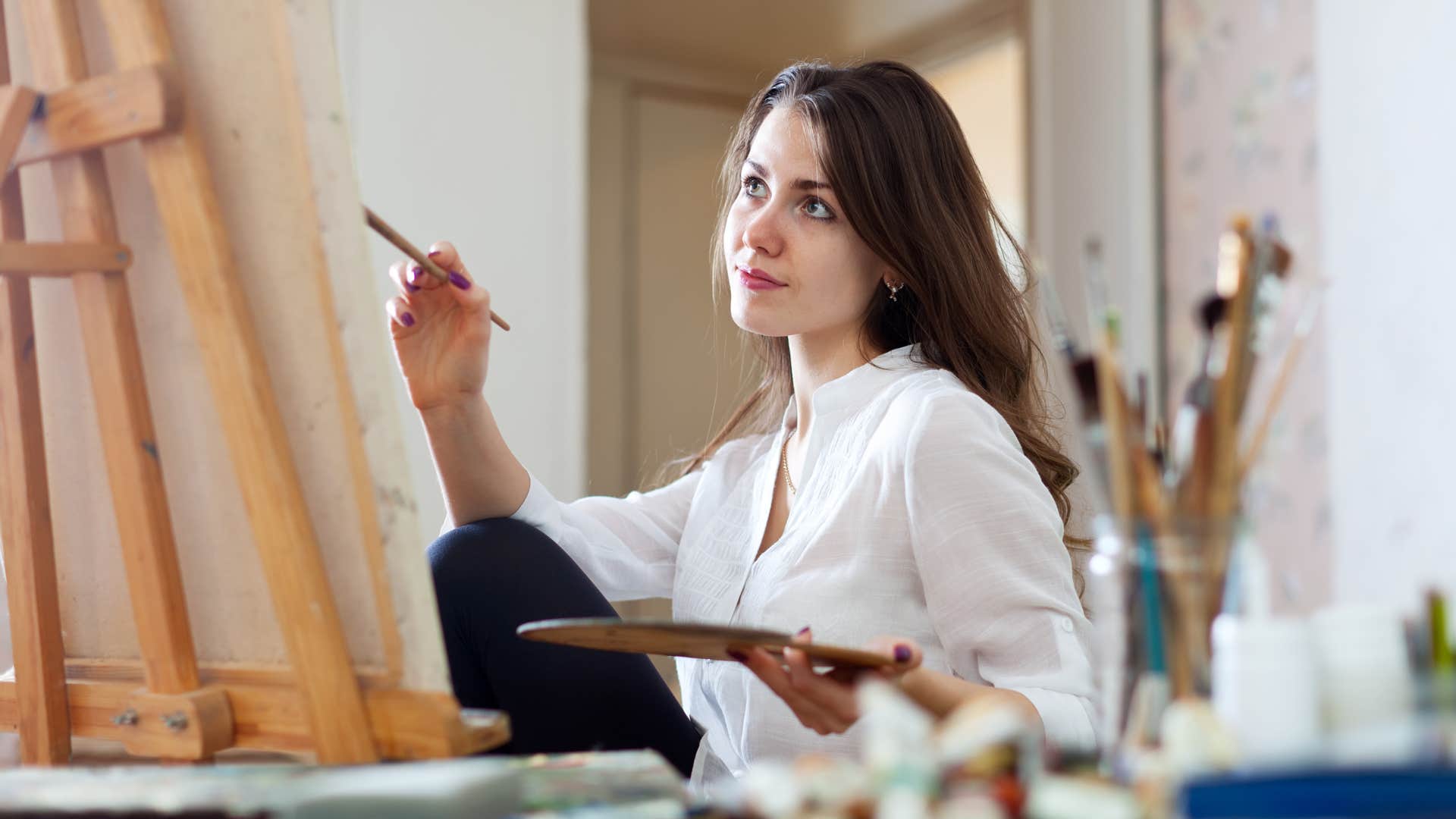 Woman smiling and painting on a canvas. 