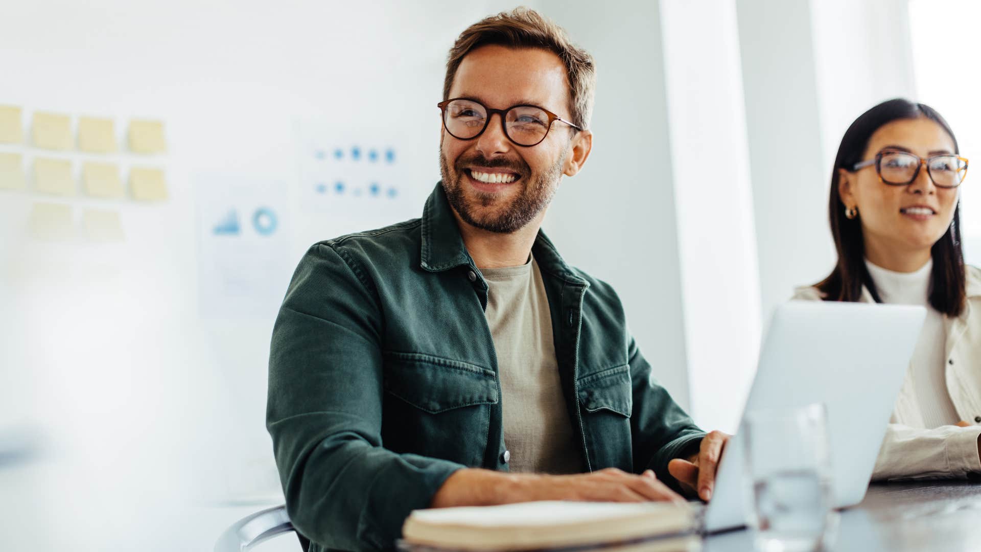 Man smiling and working on his laptop from an office. 