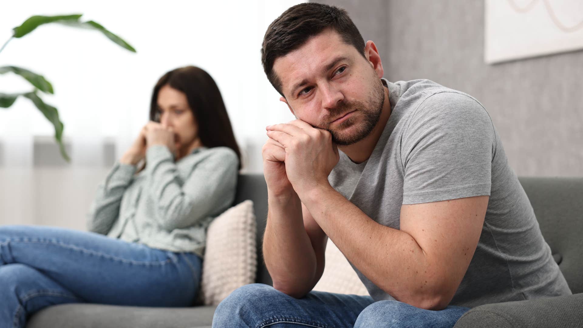 Sad man looking away from his wife on the couch