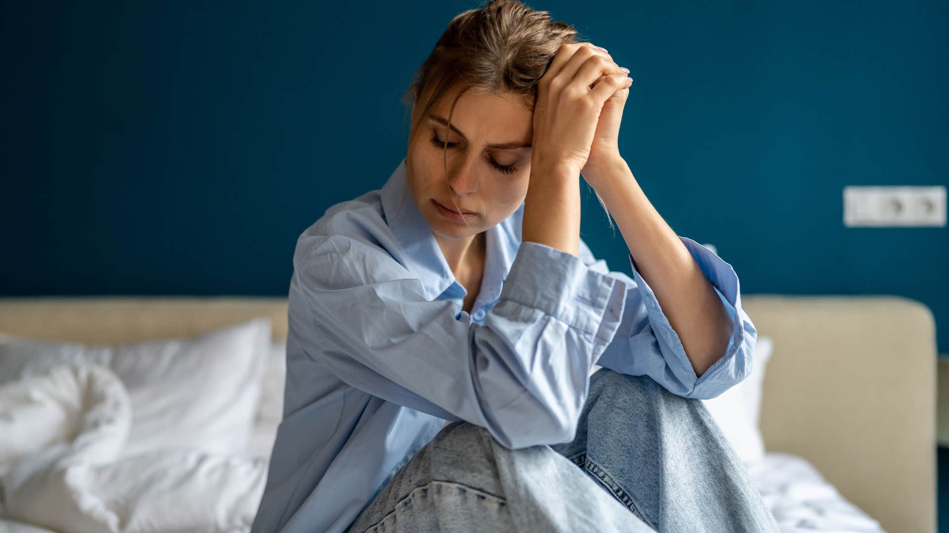 Woman looking sad sitting on her bed.